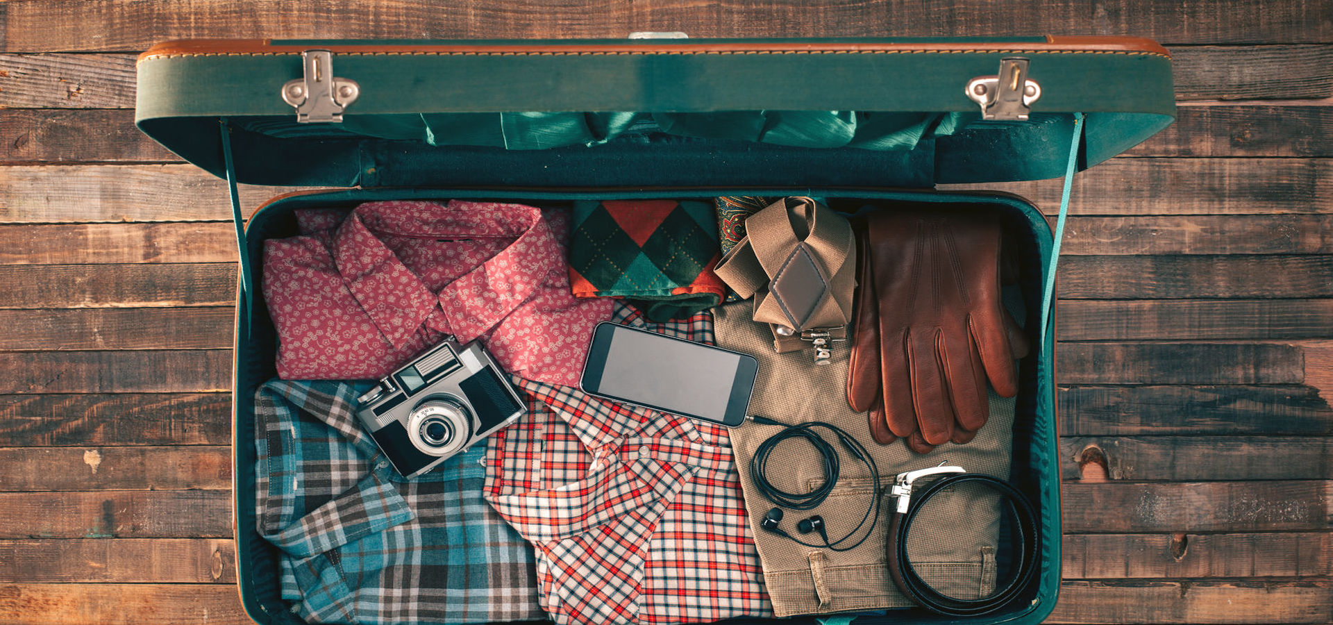 Top view of open suitcase with clothing, camera and mobile phone