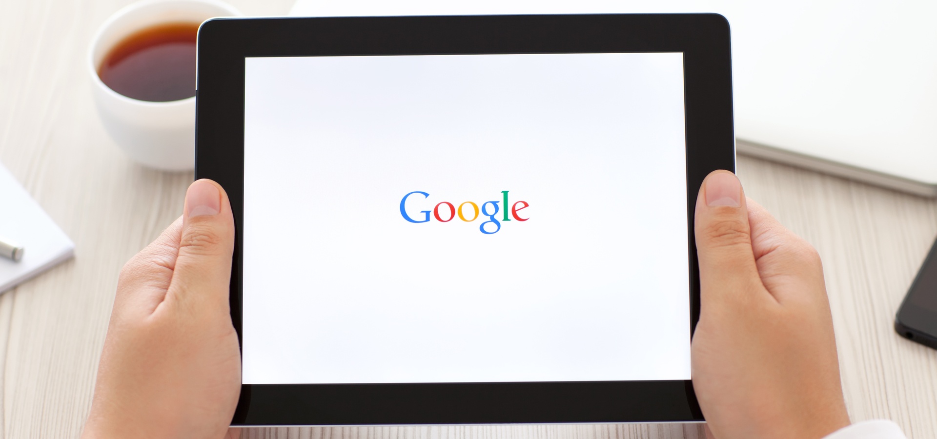 A person holding a computer tablet with the Google logo on the screen