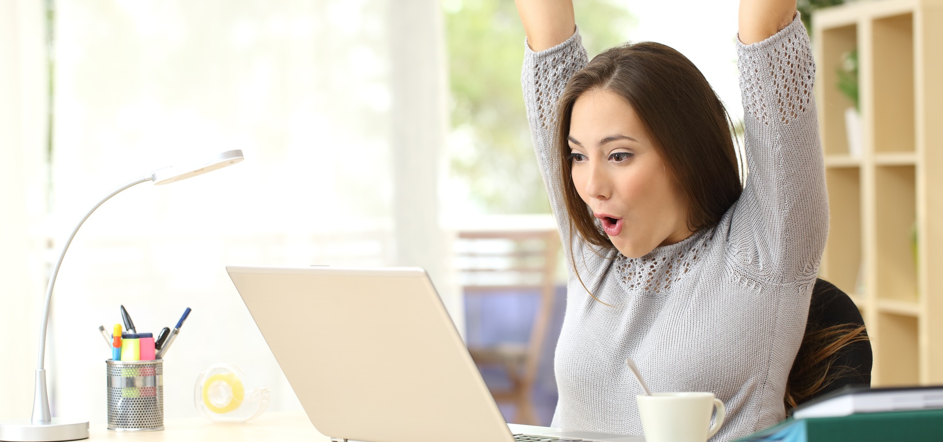Happy woman raising her arms in front of computer laptop