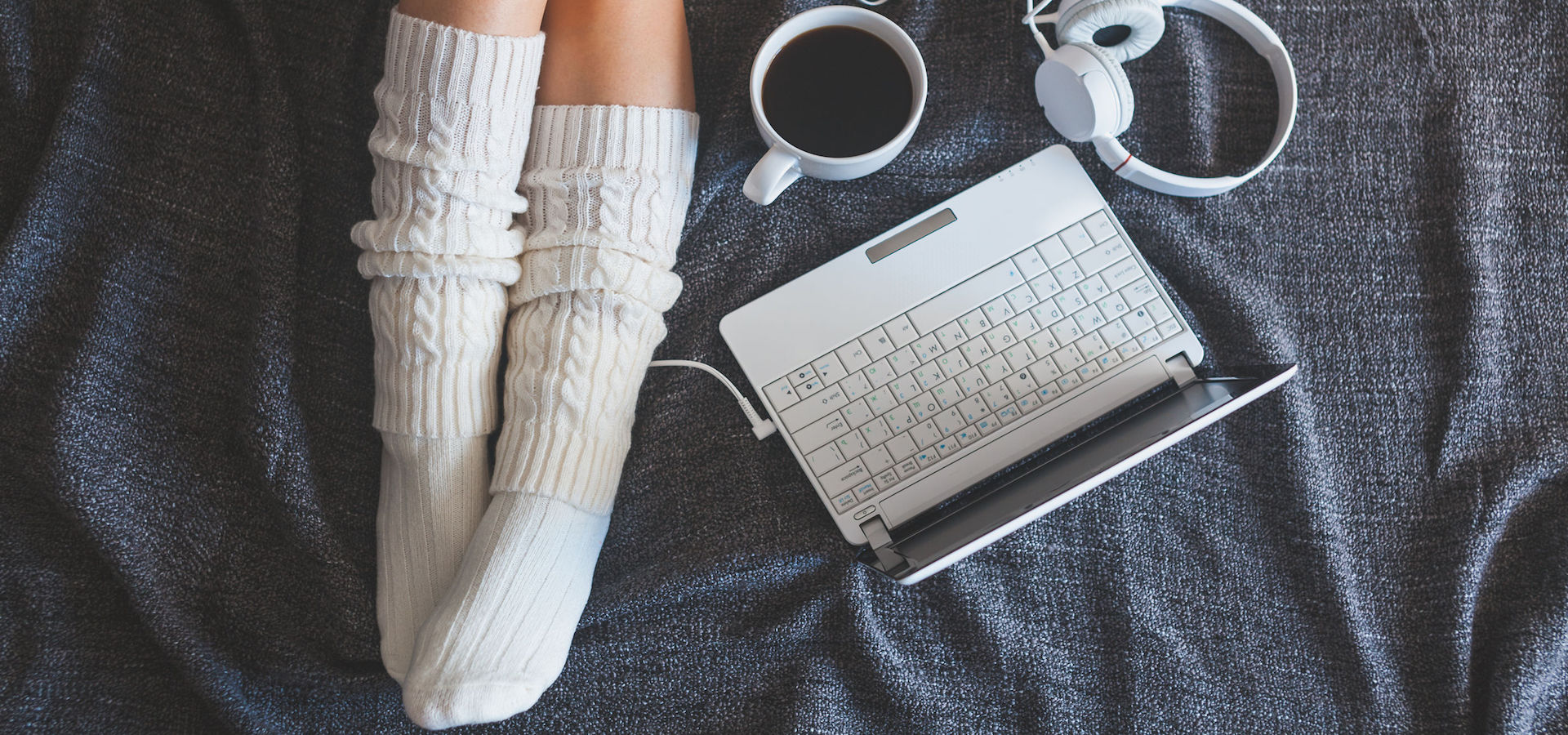 Top view of a woman's feet with a laptop, headphones and cup of coffee