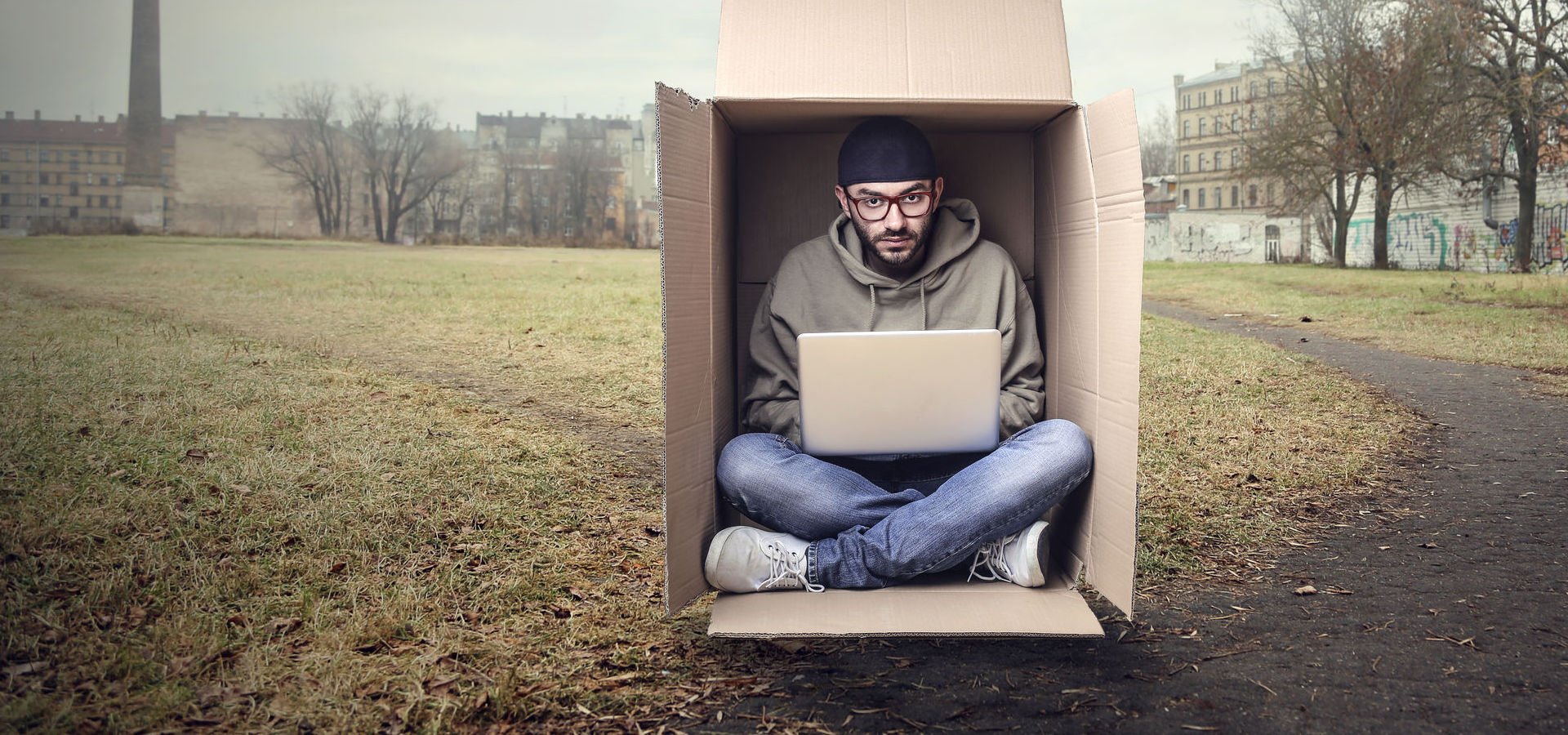 Man working on a laptop inside of a cardboard box